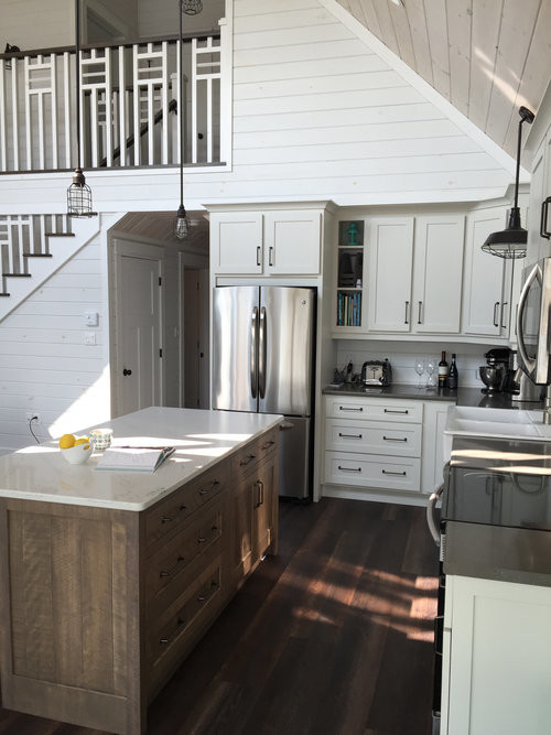 Example of a mid-sized transitional u-shaped dark wood floor and brown floor open concept kitchen design with a farmhouse sink, shaker cabinets, white cabinets, quartz countertops, white backsplash, stainless steel appliances, an island and white countertops
