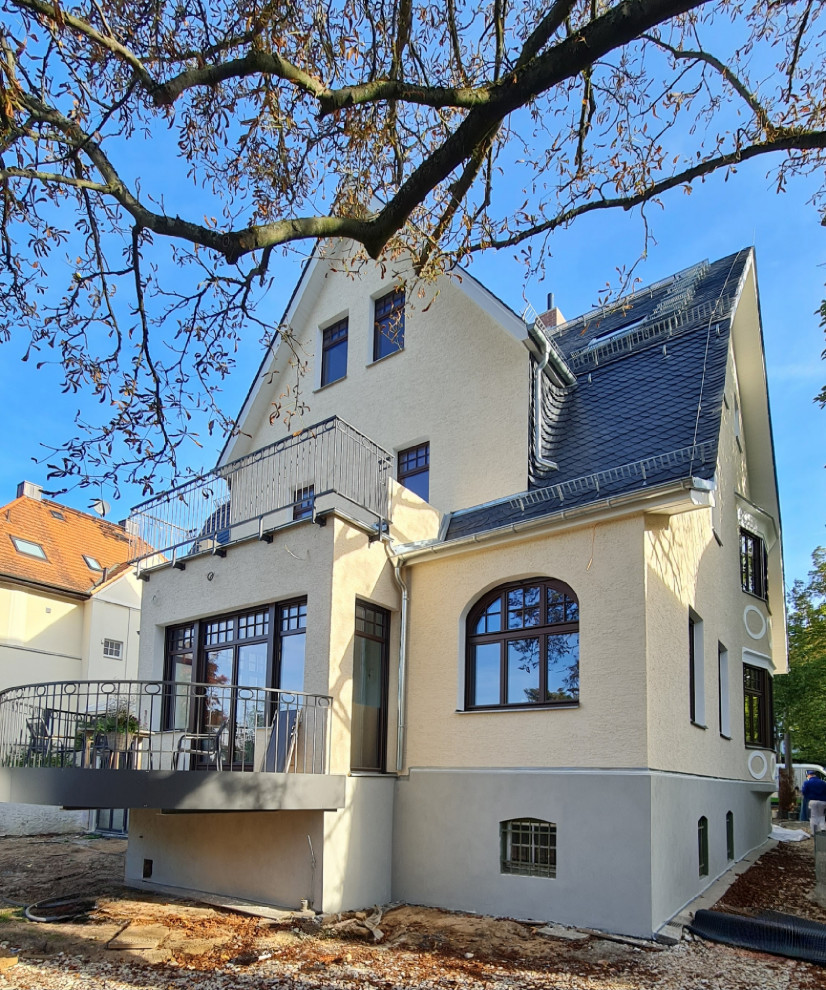 Aménagement d'une grande façade de maison beige campagne en stuc à trois étages et plus avec un toit gris.