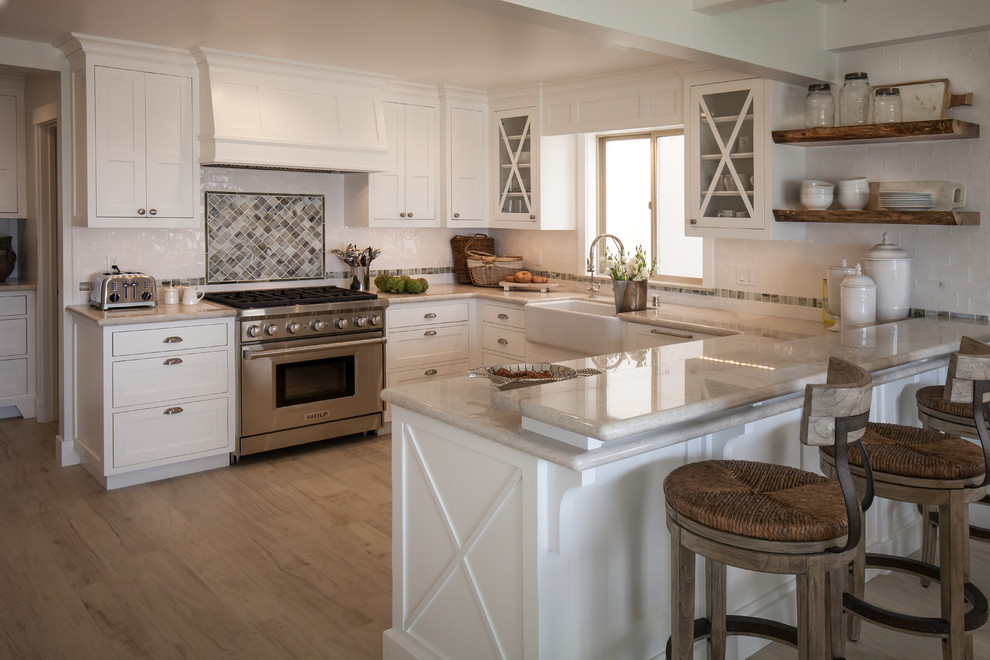 Kitchen - mid-sized coastal u-shaped kitchen idea in Los Angeles with a farmhouse sink, shaker cabinets, white cabinets, quartzite countertops, stainless steel appliances and a peninsula