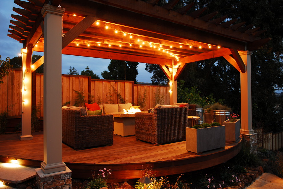 This is an example of a large eclectic backyard deck in San Francisco with a fire feature and a pergola.