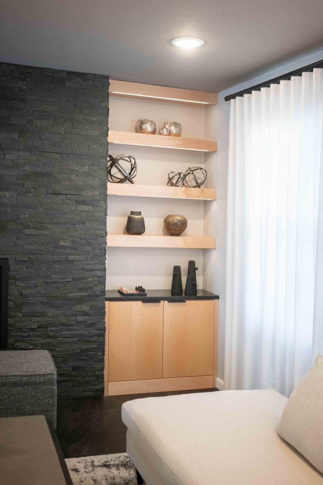 На фото: большая открытая гостиная комната в стиле ретро с серыми стенами, полом из винила, стандартным камином, фасадом камина из камня и черным полом с