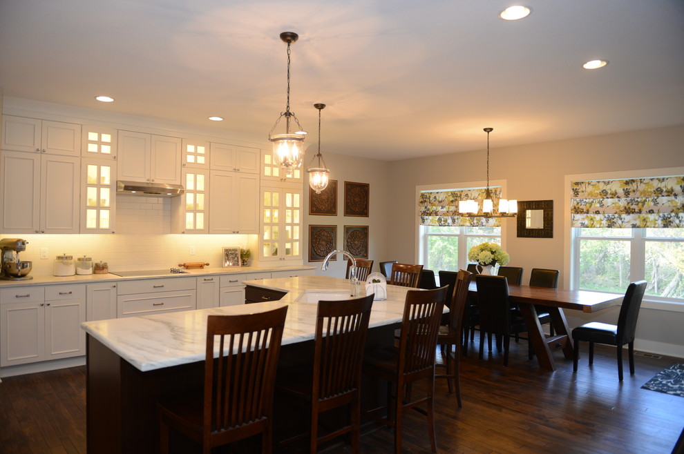 Large transitional l-shaped brown floor open concept kitchen photo with an undermount sink, recessed-panel cabinets, white cabinets, white backsplash, stainless steel appliances, an island and white countertops