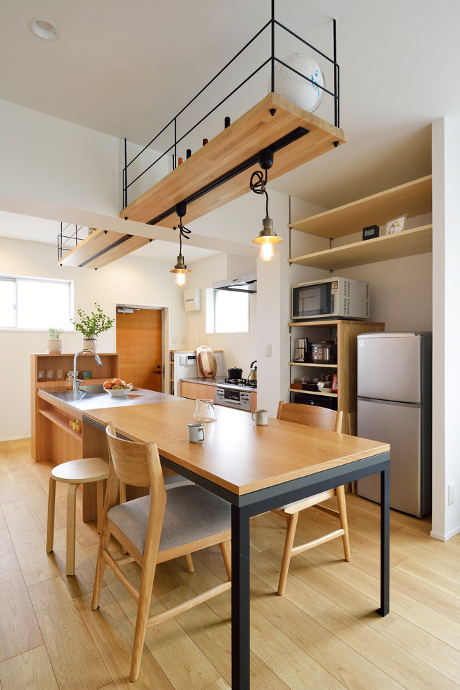 This is an example of an asian galley eat-in kitchen in Tokyo with an integrated sink, flat-panel cabinets, medium wood cabinets, stainless steel benchtops, stainless steel appliances, light hardwood floors, with island, beige floor and grey benchtop.