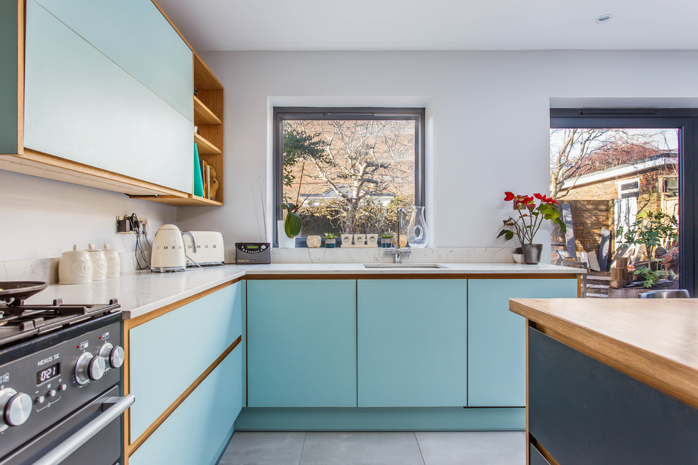 Photo of a medium sized midcentury l-shaped kitchen/diner in Sussex with a built-in sink, flat-panel cabinets, blue cabinets, quartz worktops, stainless steel appliances, an island and white worktops.