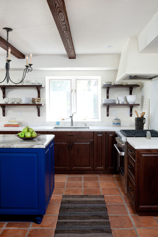 Inspiration for a large mediterranean l-shaped eat-in kitchen in Santa Barbara with raised-panel cabinets, dark wood cabinets, white splashback, terra-cotta floors, with island, stone slab splashback and stainless steel appliances.