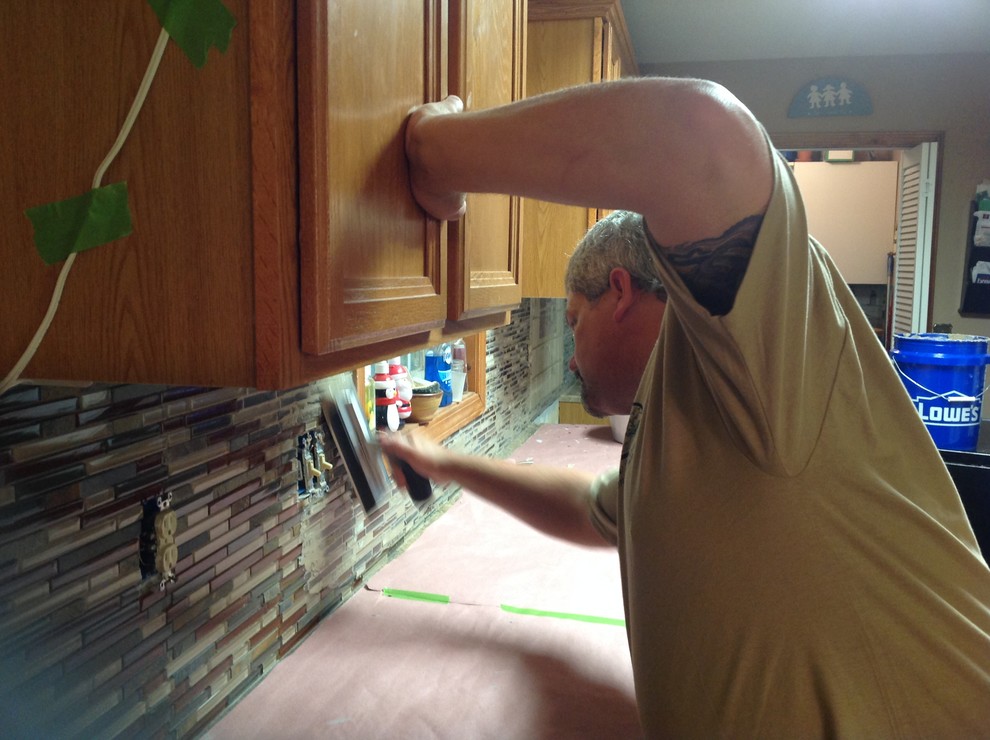 L-shaped eat-in kitchen photo with an undermount sink, flat-panel cabinets, brown backsplash, glass tile backsplash, stainless steel appliances and a peninsula