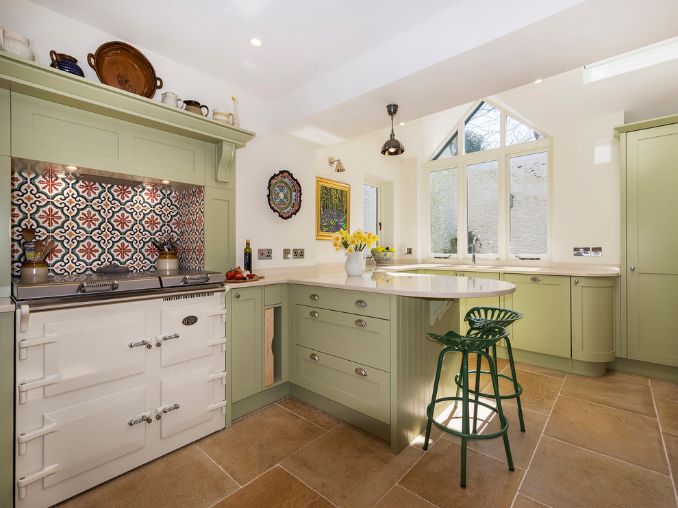 This is an example of a traditional l-shaped kitchen in Devon with shaker cabinets, green cabinets, multi-coloured splashback, mosaic tile splashback, a peninsula, brown floor, beige benchtop and white appliances.