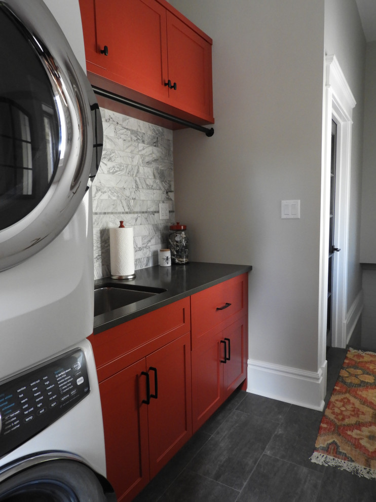 This is an example of a small transitional single-wall utility room in Toronto with an undermount sink, shaker cabinets, red cabinets, quartz benchtops, white splashback, stone tile splashback, white walls, ceramic floors, a stacked washer and dryer, grey floor, black benchtop and planked wall panelling.