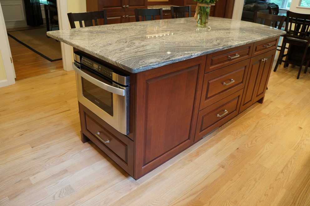 Eat-in kitchen - mid-sized transitional galley light wood floor eat-in kitchen idea in Boston with an undermount sink, raised-panel cabinets, dark wood cabinets, quartz countertops, white backsplash, ceramic backsplash, stainless steel appliances and an island