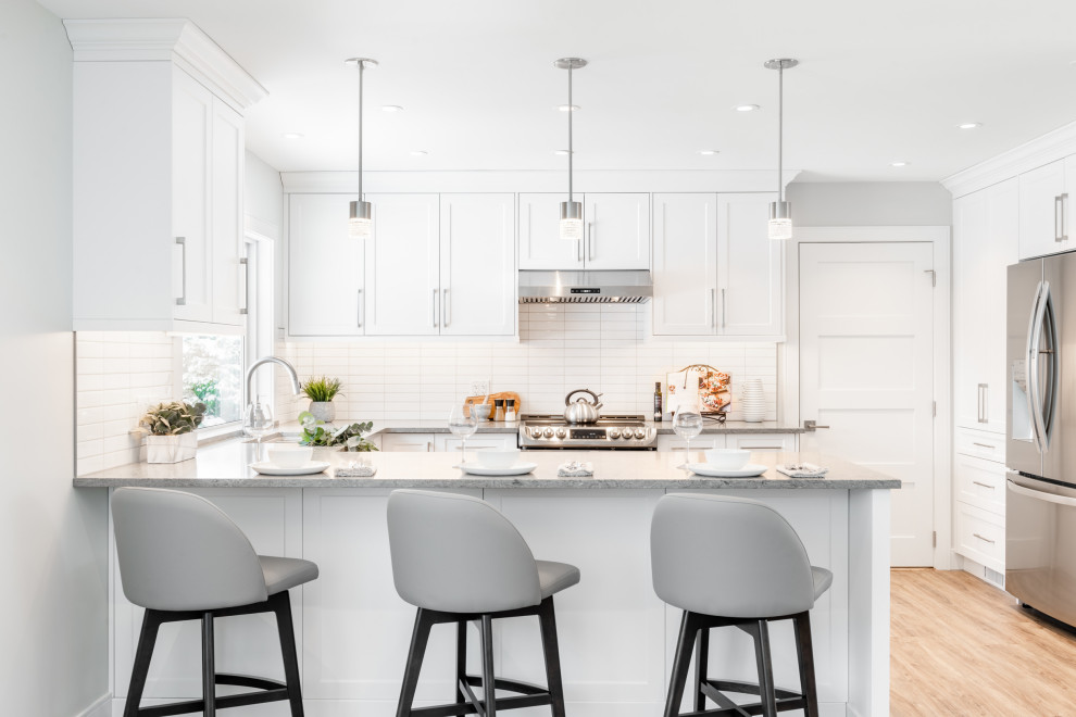 Photo of a mid-sized transitional u-shaped open plan kitchen in Vancouver with an undermount sink, shaker cabinets, white cabinets, quartz benchtops, white splashback, subway tile splashback, stainless steel appliances, vinyl floors, a peninsula, beige floor and grey benchtop.