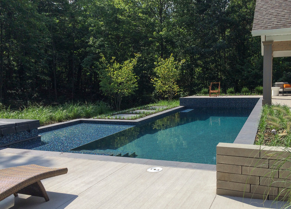 Expansive contemporary backyard custom-shaped lap pool in Grand Rapids with a pool house and tile.