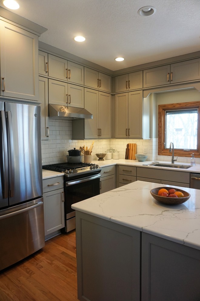 Eat-in kitchen - transitional l-shaped medium tone wood floor eat-in kitchen idea with an undermount sink, recessed-panel cabinets, gray cabinets, quartz countertops, white backsplash, ceramic backsplash, stainless steel appliances, an island and white countertops