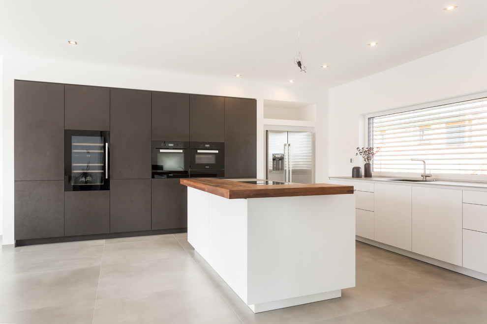 Large contemporary l-shaped open plan kitchen in Frankfurt with an integrated sink, flat-panel cabinets, white cabinets, solid surface benchtops, window splashback, black appliances, with island, grey floor and grey benchtop.