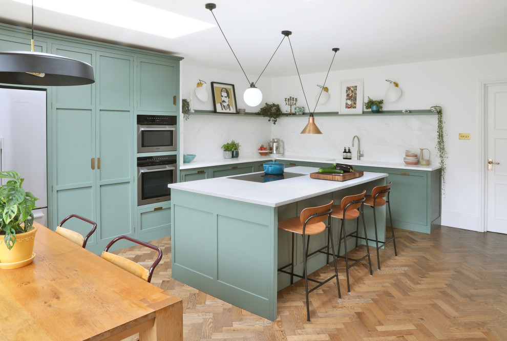 Design ideas for a mid-sized transitional l-shaped eat-in kitchen in London with an integrated sink, shaker cabinets, green cabinets, quartzite benchtops, white splashback, engineered quartz splashback, stainless steel appliances, medium hardwood floors, with island, brown floor and white benchtop.