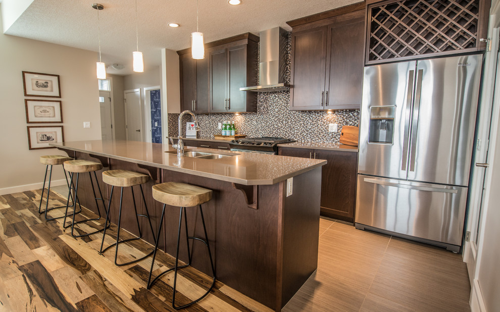 Photo of a mid-sized country galley open plan kitchen in Calgary with an undermount sink, shaker cabinets, medium wood cabinets, quartz benchtops, multi-coloured splashback, mosaic tile splashback, stainless steel appliances, medium hardwood floors and with island.