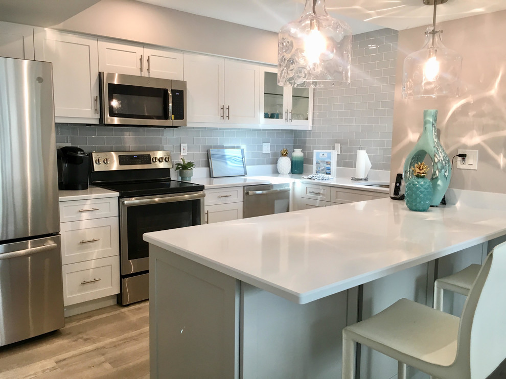 Photo of a small beach style galley eat-in kitchen in Tampa with an undermount sink, shaker cabinets, grey cabinets, quartzite benchtops, glass tile splashback, stainless steel appliances, vinyl floors, a peninsula, grey floor and white benchtop.