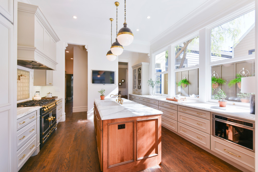 This is an example of a mid-sized traditional galley eat-in kitchen in San Francisco with an undermount sink, flat-panel cabinets, grey cabinets, quartzite benchtops, white splashback, subway tile splashback, black appliances, medium hardwood floors, with island, brown floor and white benchtop.