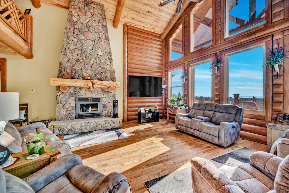Photo of a large country open concept living room in Other with brown walls, light hardwood floors, a standard fireplace, a stone fireplace surround, a wall-mounted tv, brown floor, vaulted and wood walls.
