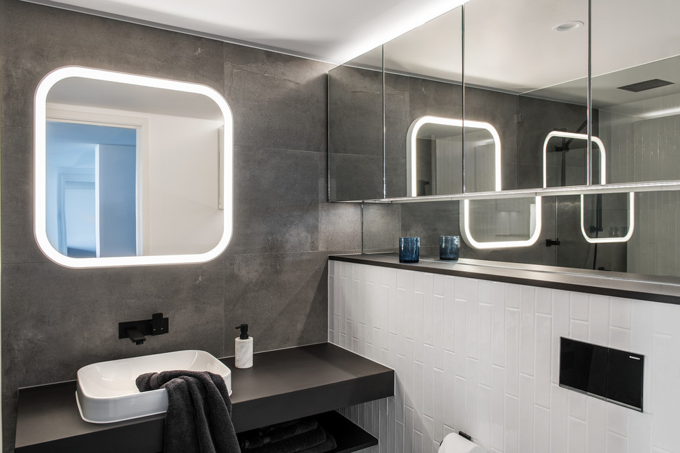 Inspiration for a small 3/4 bathroom in Other with flat-panel cabinets, a curbless shower, a two-piece toilet, black and white tile, ceramic tile, grey walls, porcelain floors, a vessel sink, solid surface benchtops, grey floor, an open shower and black benchtops.