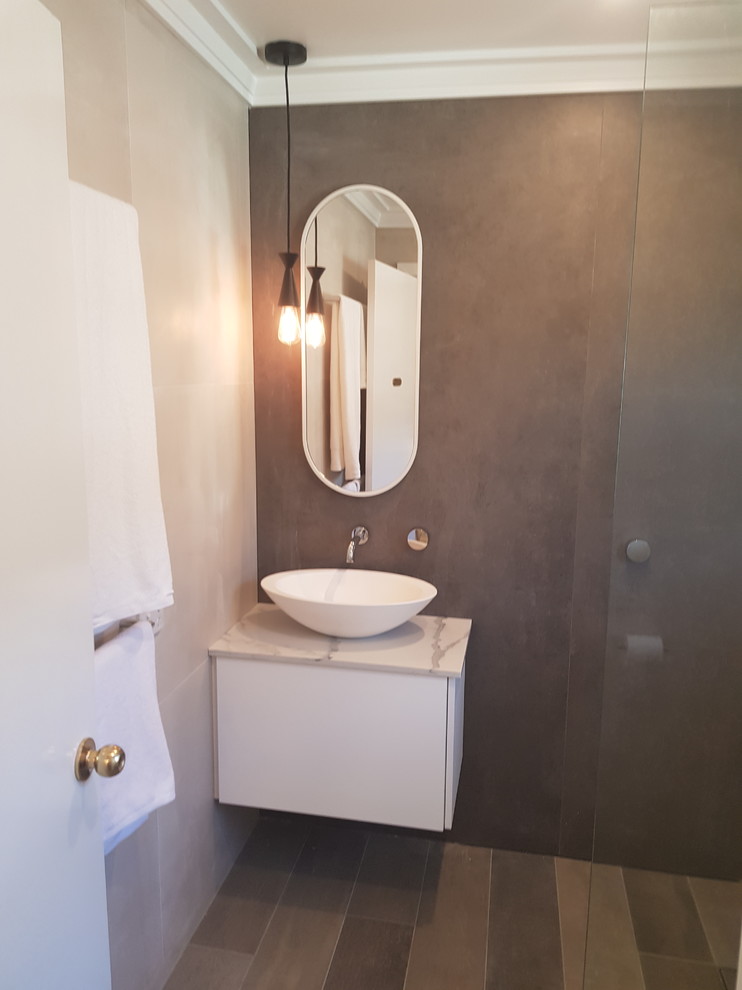This is an example of a mid-sized contemporary bathroom in Sydney with flat-panel cabinets, white cabinets, a corner shower, a wall-mount toilet, brown tile, porcelain tile, brown walls, porcelain floors, a vessel sink, engineered quartz benchtops, brown floor, an open shower and white benchtops.