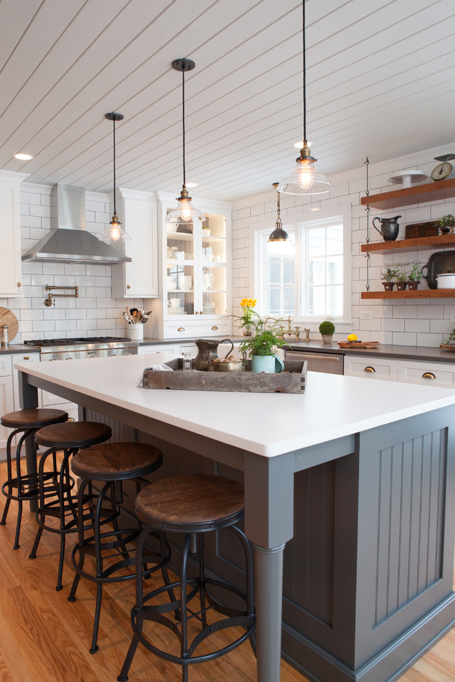 This is an example of a mid-sized transitional u-shaped eat-in kitchen in Chicago with a farmhouse sink, recessed-panel cabinets, white cabinets, quartz benchtops, multi-coloured splashback, subway tile splashback, stainless steel appliances, light hardwood floors and with island.