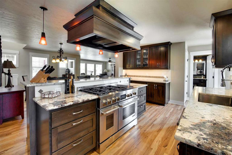 This is an example of a mid-sized transitional galley eat-in kitchen in Boise with a single-bowl sink, shaker cabinets, dark wood cabinets, granite benchtops, white splashback, ceramic splashback, stainless steel appliances, light hardwood floors and with island.