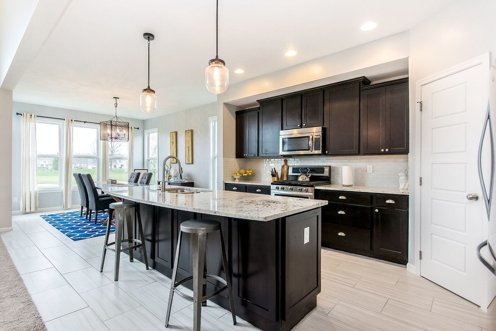 Example of a mid-sized transitional l-shaped porcelain tile and beige floor open concept kitchen design in Columbus with a double-bowl sink, shaker cabinets, dark wood cabinets, granite countertops, white backsplash, glass tile backsplash, stainless steel appliances and an island