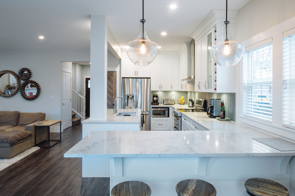 This is an example of a large modern l-shaped eat-in kitchen in Vancouver with an undermount sink, shaker cabinets, white cabinets, glass benchtops, grey splashback, glass sheet splashback, stainless steel appliances, laminate floors, with island and grey floor.