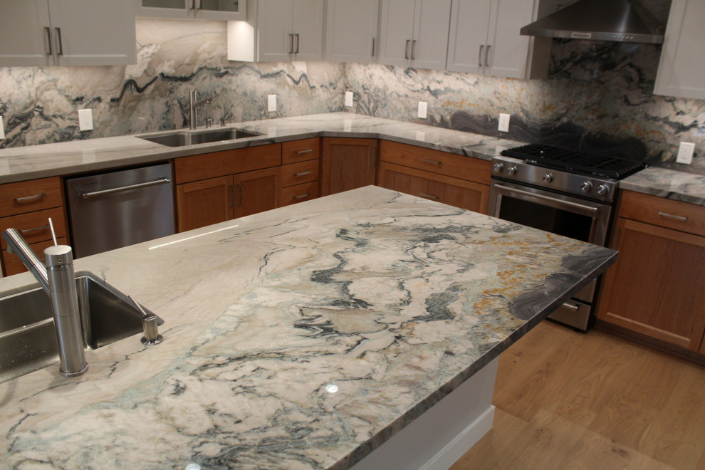 Large transitional l-shaped medium tone wood floor, brown floor and vaulted ceiling kitchen photo in San Francisco with an undermount sink, shaker cabinets, medium tone wood cabinets, granite countertops, multicolored backsplash, stone slab backsplash, stainless steel appliances, an island and multicolored countertops