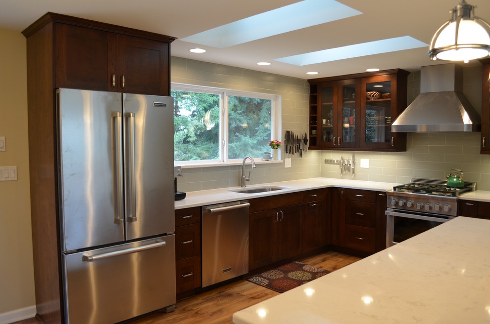 Inspiration for a mid-sized transitional l-shaped medium tone wood floor and brown floor open concept kitchen remodel in Seattle with an undermount sink, shaker cabinets, dark wood cabinets, quartz countertops, stainless steel appliances, an island, gray backsplash and subway tile backsplash