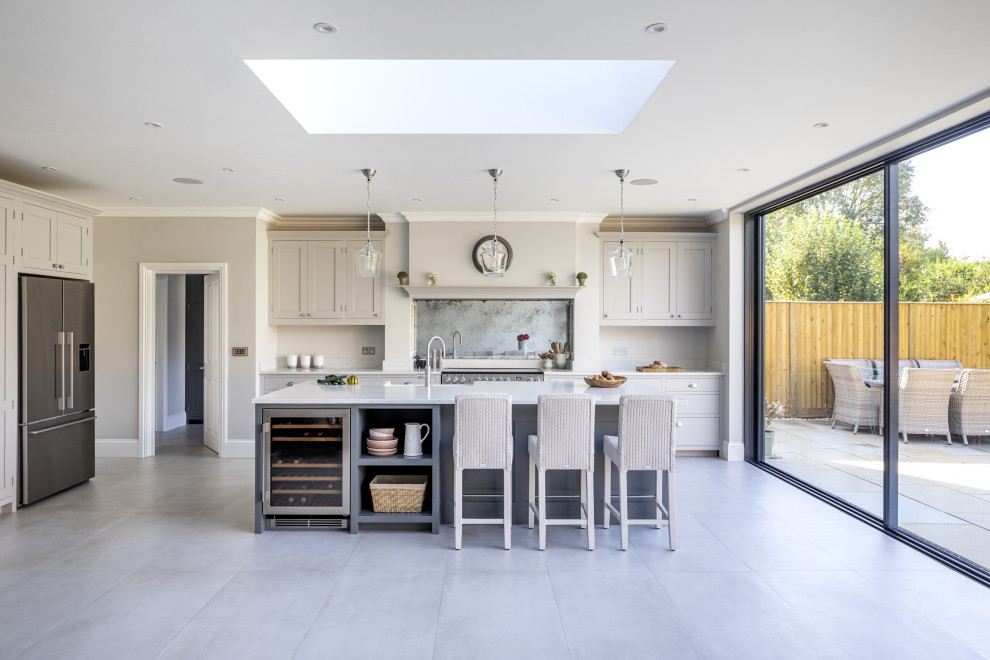 Design ideas for a mid-sized transitional l-shaped eat-in kitchen in Surrey with a farmhouse sink, shaker cabinets, grey cabinets, quartzite benchtops, grey splashback, mirror splashback, stainless steel appliances, porcelain floors, with island, grey floor and white benchtop.