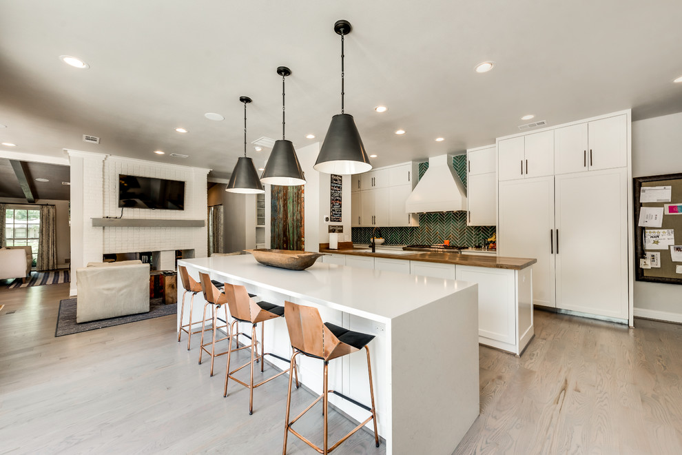This is an example of a contemporary single-wall open plan kitchen in Dallas with a double-bowl sink, shaker cabinets, white cabinets, solid surface benchtops, green splashback, ceramic splashback, stainless steel appliances, light hardwood floors, multiple islands and brown floor.