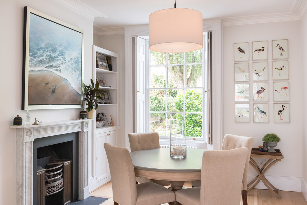 Photo of a transitional dining room in London with beige walls, light hardwood floors and a standard fireplace.