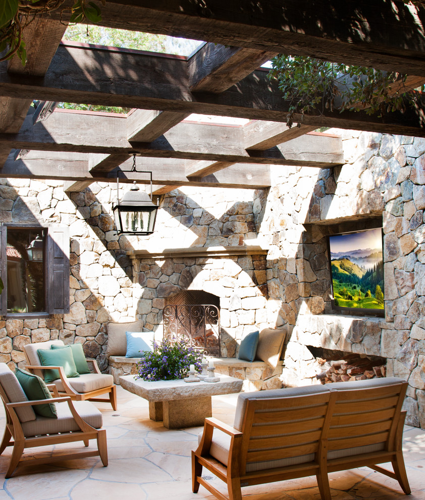 This is an example of a mediterranean courtyard patio in San Diego with natural stone pavers, a pergola and with fireplace.