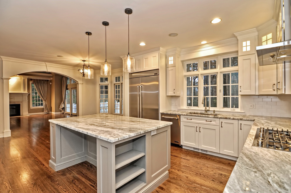 Eat-in kitchen - large transitional l-shaped medium tone wood floor and brown floor eat-in kitchen idea in Boston with an undermount sink, shaker cabinets, white cabinets, granite countertops, white backsplash, porcelain backsplash, stainless steel appliances, an island and multicolored countertops