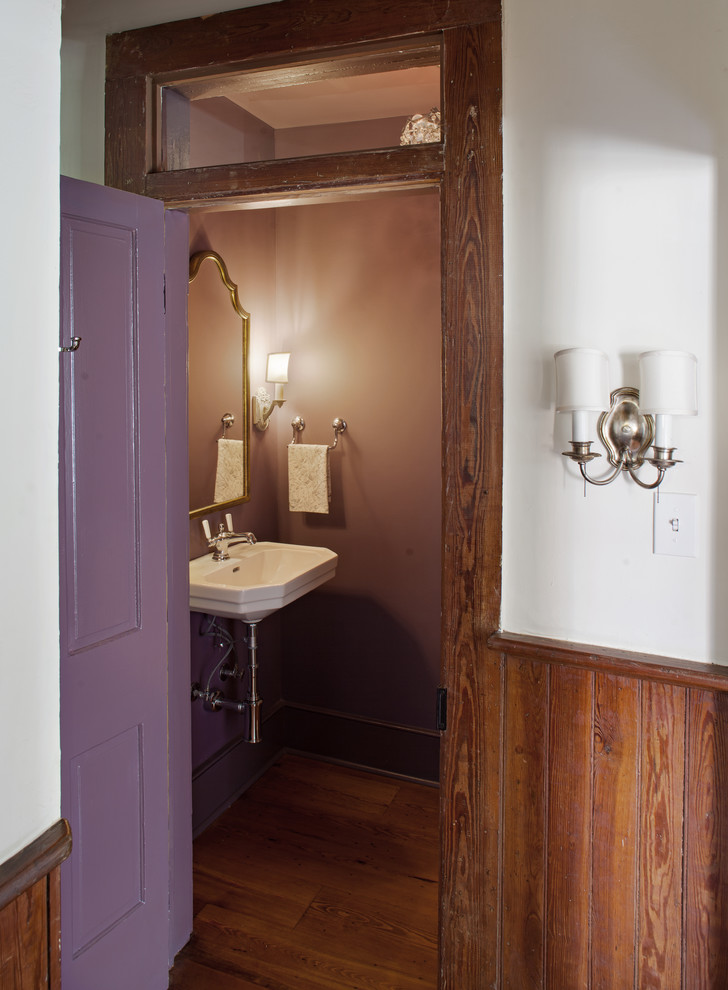 Inspiration for a small country powder room in Atlanta with a two-piece toilet, purple walls, medium hardwood floors, a wall-mount sink and brown floor.