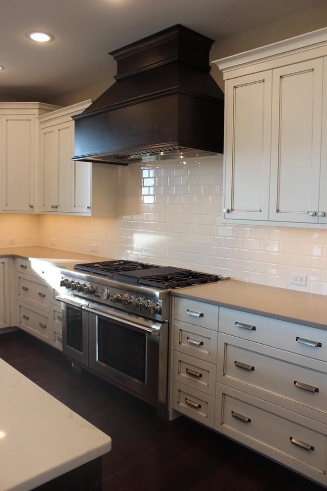 Enclosed kitchen - large transitional l-shaped dark wood floor enclosed kitchen idea with a farmhouse sink, shaker cabinets, white cabinets, quartz countertops, white backsplash, subway tile backsplash, stainless steel appliances and an island
