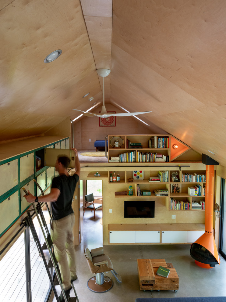 Modelo de sala de estar con biblioteca tipo loft rústica pequeña con suelo de cemento, estufa de leña, televisor colgado en la pared, suelo gris, madera y madera