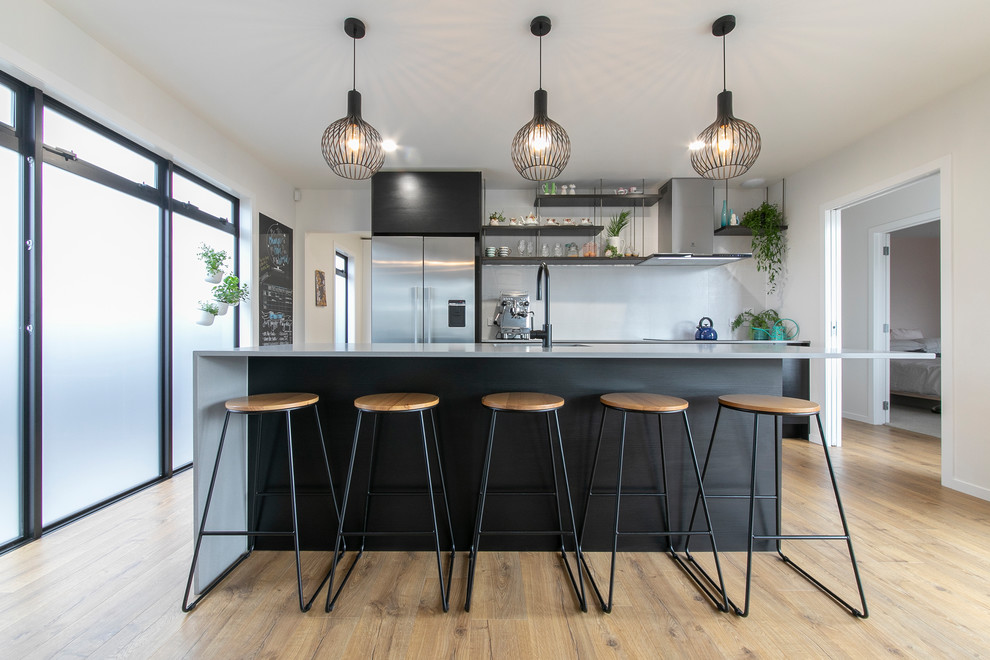 This is an example of a large contemporary galley eat-in kitchen in Auckland with a single-bowl sink, flat-panel cabinets, black cabinets, quartz benchtops, white splashback, stainless steel appliances, laminate floors, with island, grey benchtop and beige floor.