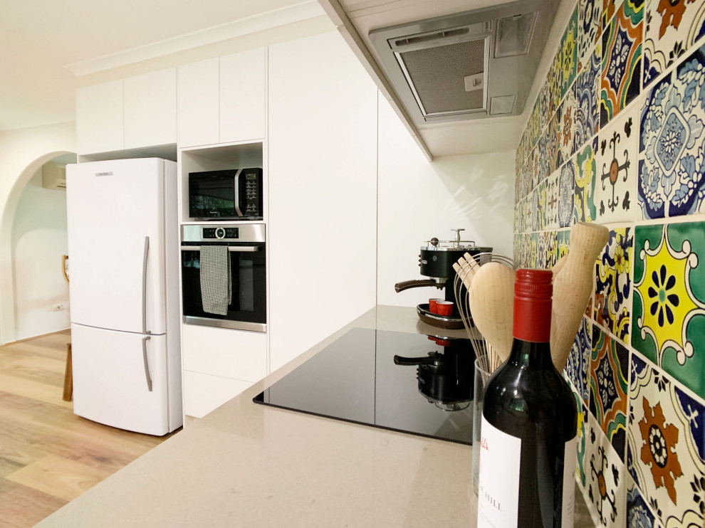 Photo of a mid-sized transitional u-shaped separate kitchen in Brisbane with a single-bowl sink, shaker cabinets, white cabinets, quartz benchtops, multi-coloured splashback, mosaic tile splashback, stainless steel appliances, light hardwood floors, a peninsula, brown floor and brown benchtop.