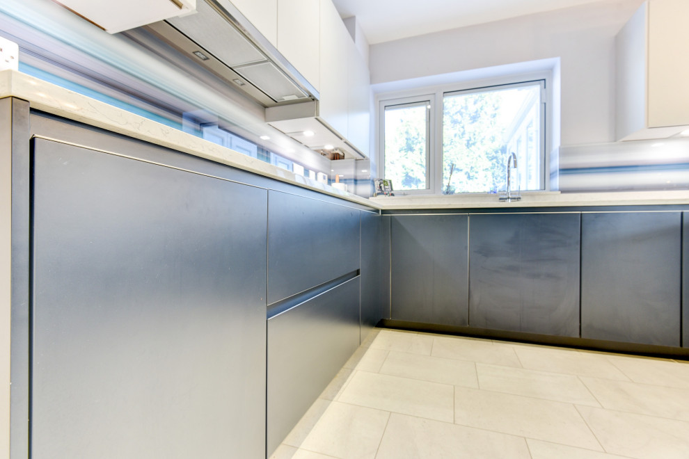 Inspiration for a large modern u-shaped eat-in kitchen in Sussex with an undermount sink, flat-panel cabinets, blue cabinets, quartzite benchtops, blue splashback, glass sheet splashback, black appliances, vinyl floors, a peninsula, white floor and white benchtop.