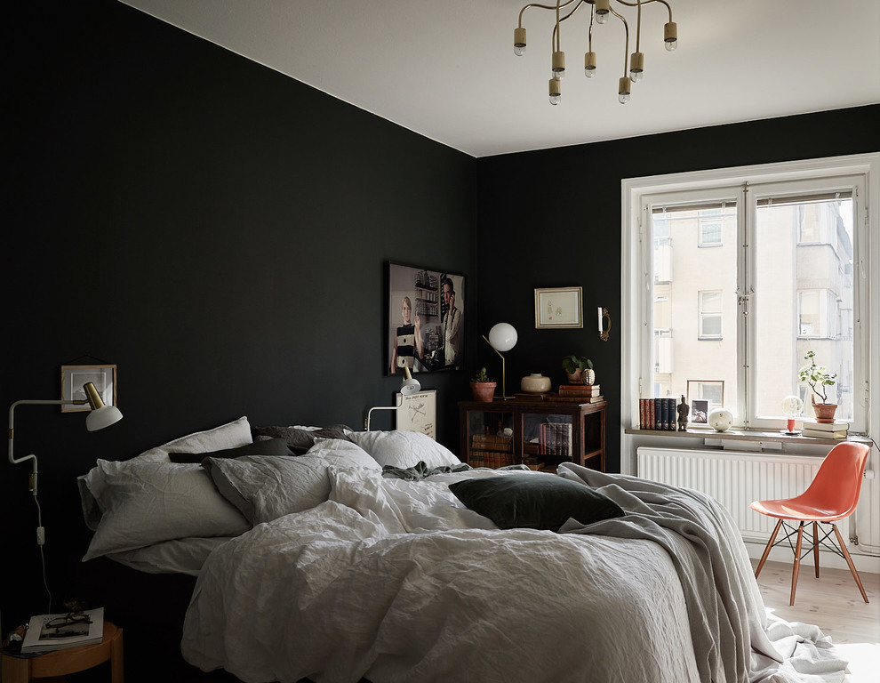 Industrial master bedroom in Stockholm with black walls, light hardwood floors and no fireplace.