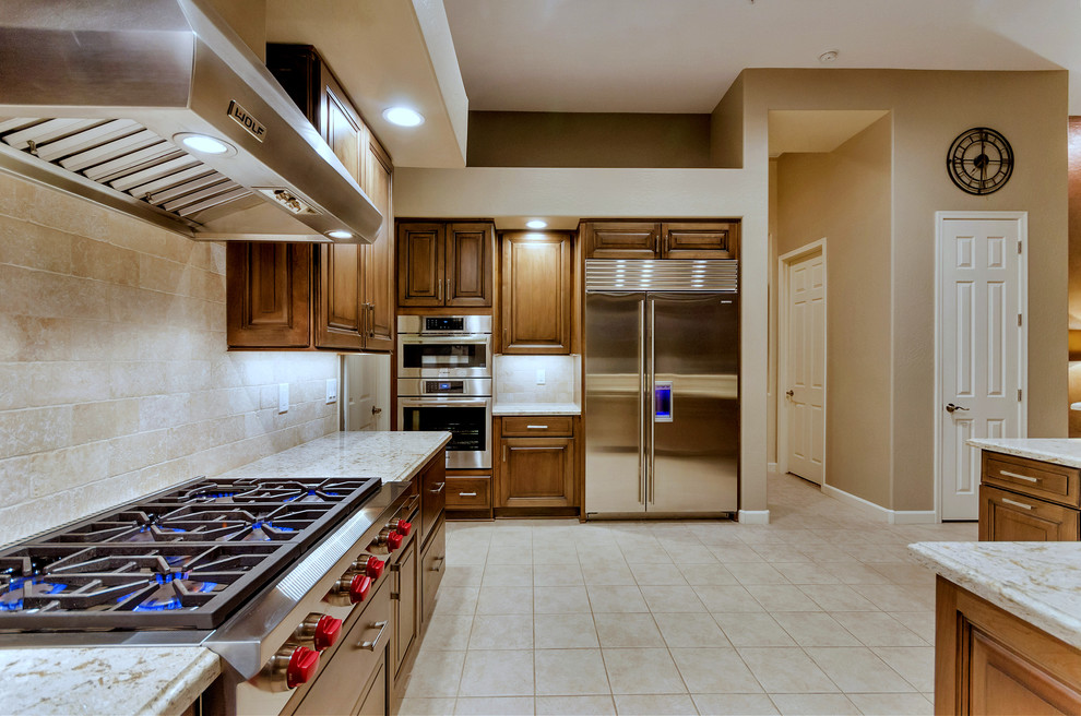 Large transitional l-shaped ceramic tile and white floor open concept kitchen photo in Phoenix with an undermount sink, raised-panel cabinets, medium tone wood cabinets, solid surface countertops, white backsplash, stainless steel appliances and an island