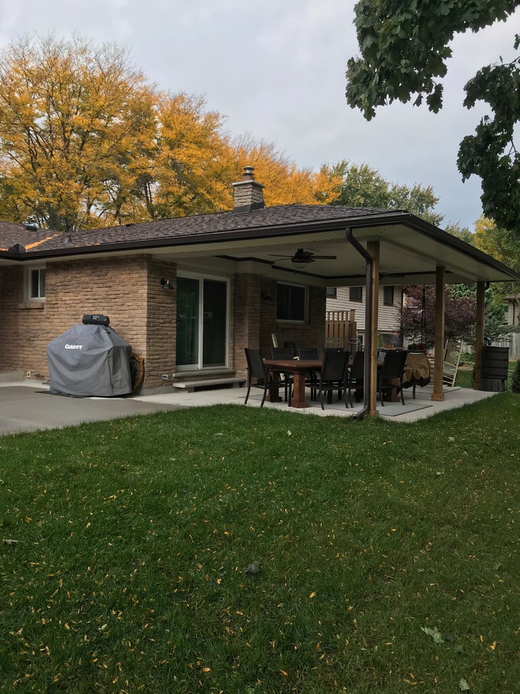 This is an example of a large traditional backyard verandah in Toronto with a fire feature, concrete slab and a roof extension.