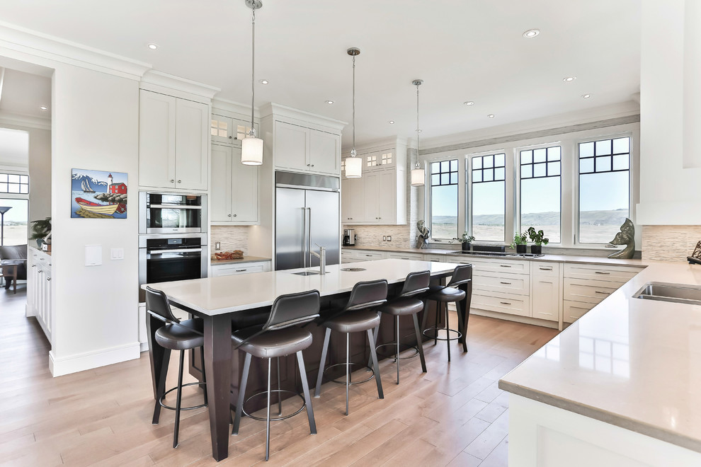 Example of a transitional u-shaped light wood floor kitchen design in Calgary with a drop-in sink, shaker cabinets, white cabinets, beige backsplash, matchstick tile backsplash, stainless steel appliances, an island and beige countertops