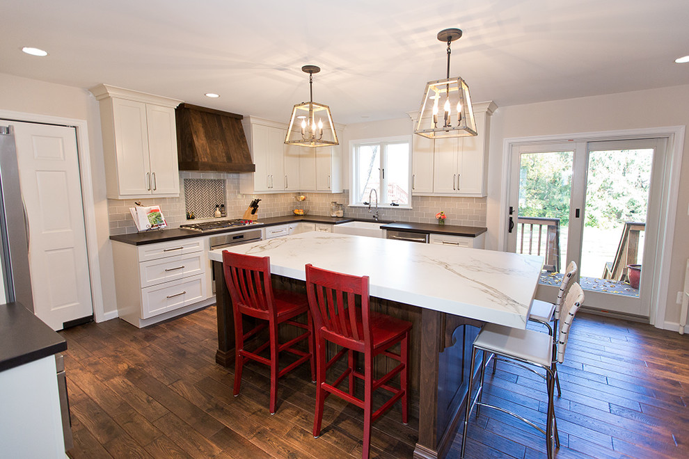 This is an example of a large transitional u-shaped eat-in kitchen in DC Metro with a farmhouse sink, shaker cabinets, white cabinets, quartz benchtops, grey splashback, subway tile splashback, stainless steel appliances, dark hardwood floors and with island.