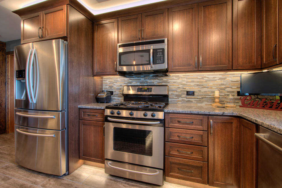 This is an example of a large country l-shaped kitchen pantry in Milwaukee with an undermount sink, flat-panel cabinets, medium wood cabinets, granite benchtops, beige splashback, ceramic splashback, stainless steel appliances, porcelain floors and with island.