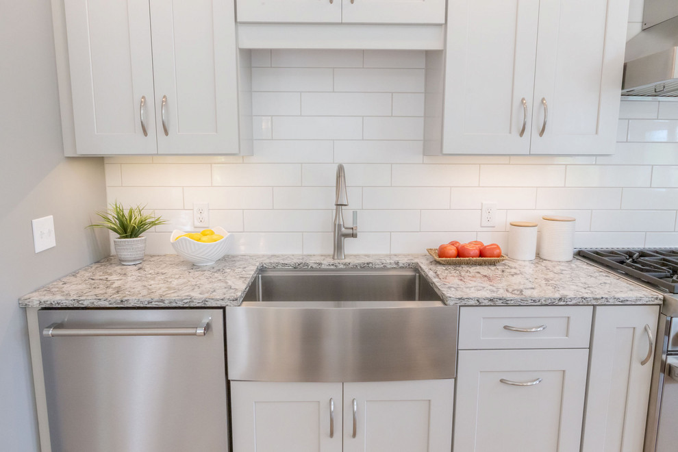 This is an example of a large transitional galley eat-in kitchen in Burlington with a farmhouse sink, shaker cabinets, grey cabinets, quartz benchtops, white splashback, subway tile splashback, stainless steel appliances, light hardwood floors, with island, beige floor and grey benchtop.