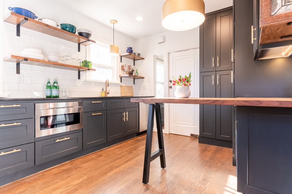 Photo of a small contemporary galley separate kitchen in Denver with an undermount sink, shaker cabinets, black cabinets, quartzite benchtops, white splashback, ceramic splashback, stainless steel appliances, dark hardwood floors, a peninsula, brown floor and black benchtop.