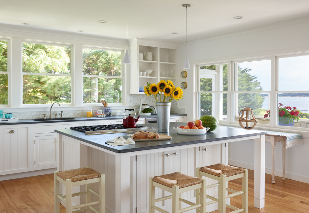Beach style kitchen in Boston with an undermount sink, recessed-panel cabinets, white cabinets, white splashback, mosaic tile splashback, stainless steel appliances, medium hardwood floors, with island, brown floor and grey benchtop.
